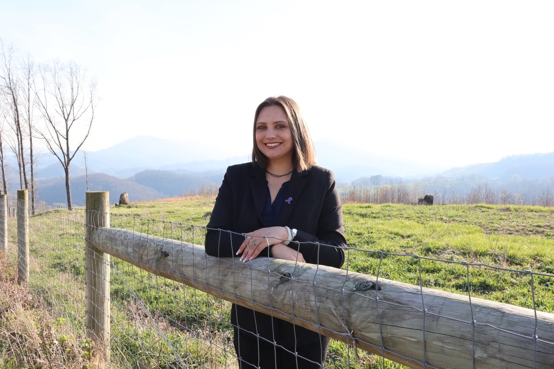 Olivia McKinney, Founder and Owner of Appalachian Meridian Group, standing by a fence with the Appalachian mountains behind her